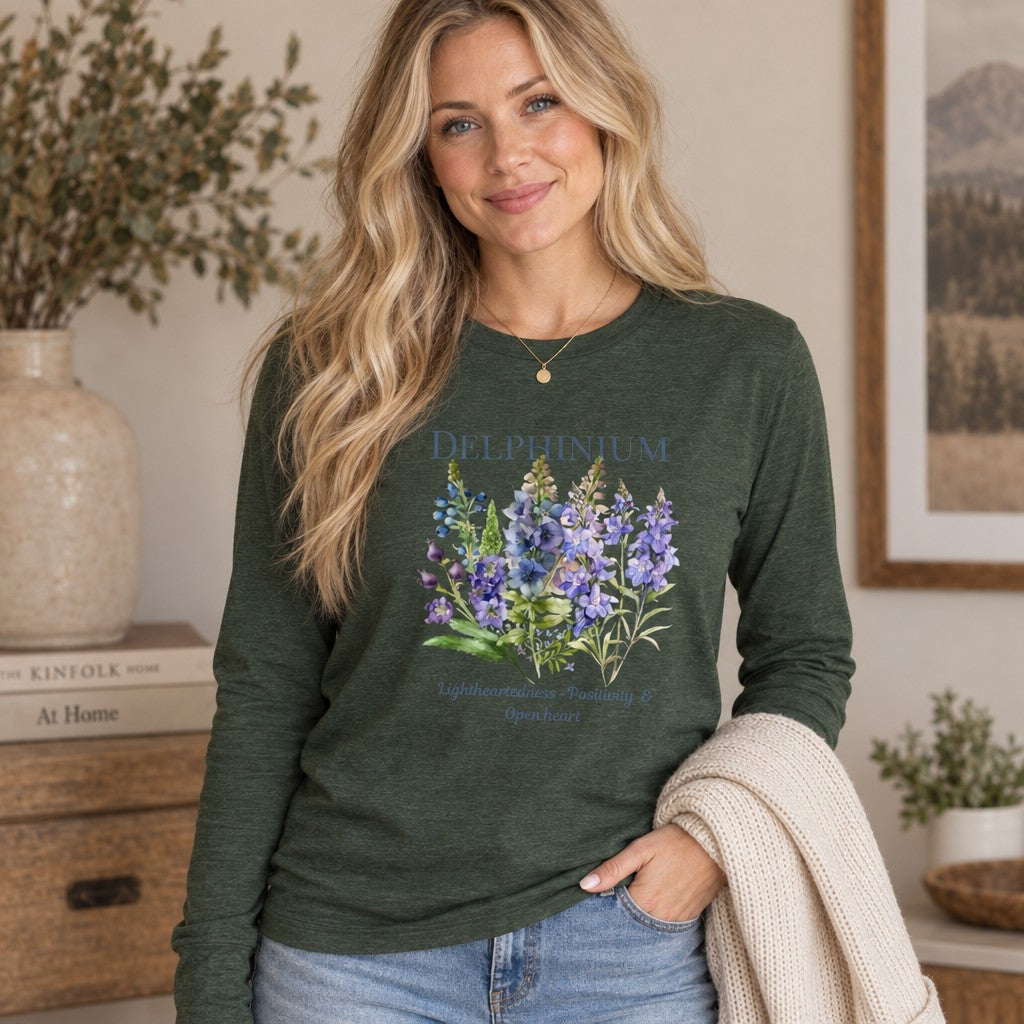 Woman in heather forest Bella Canvas 3501 long sleeve shirt featuring a vintage-inspired watercolor larkspur floral design, cottagecore style, cozy indoor setting, plant lovers, by Crossroads Dandelion