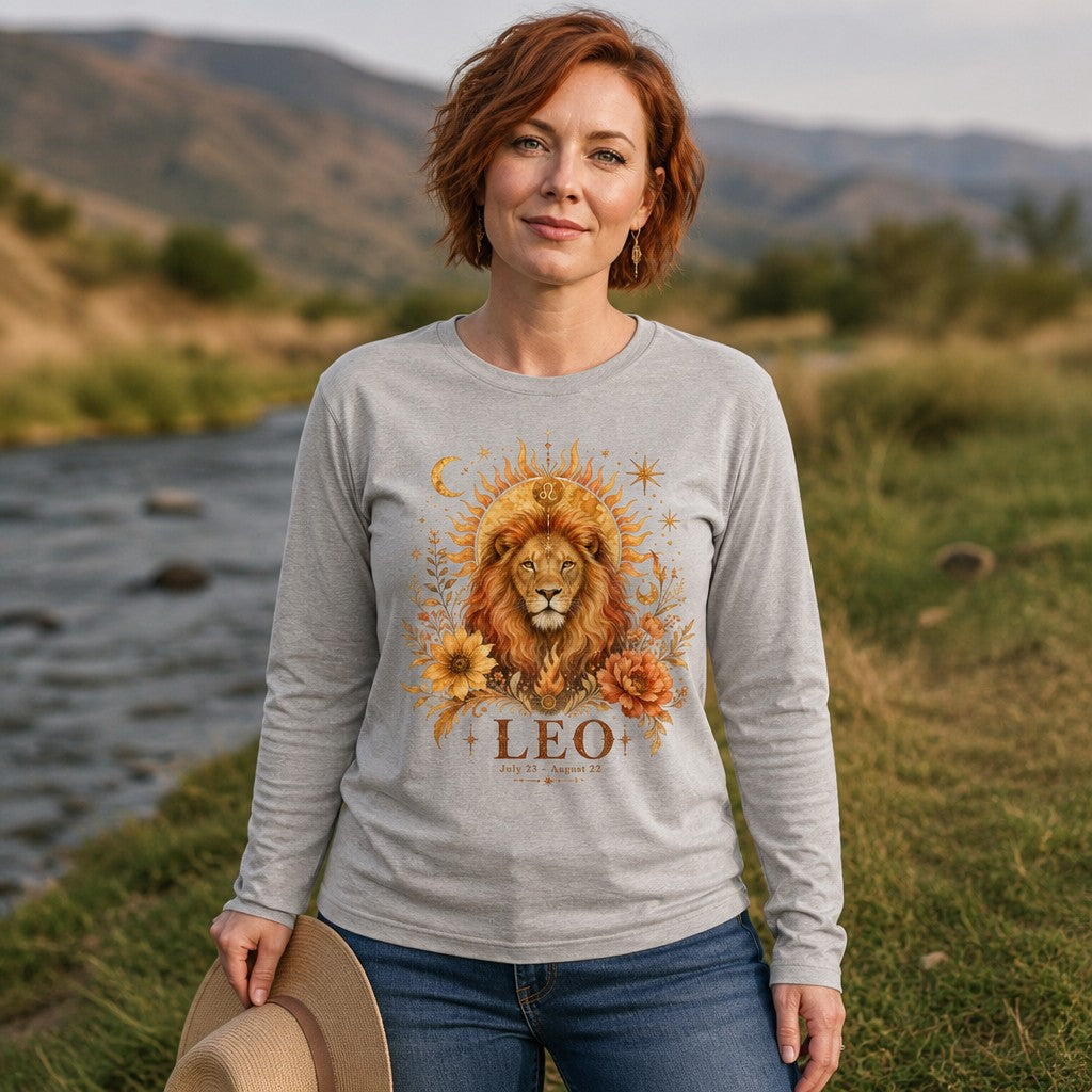 Woman in athletic heather Bella Canvas 3501 long sleeve shirt featuring a cottagecore hand-painted regal lion with Leo zodiac glyph, golden sunbeams, moons, and lush florals, standing by a riverside, ideal for astrology and botanical art lovers, by Crossroads Dandelion