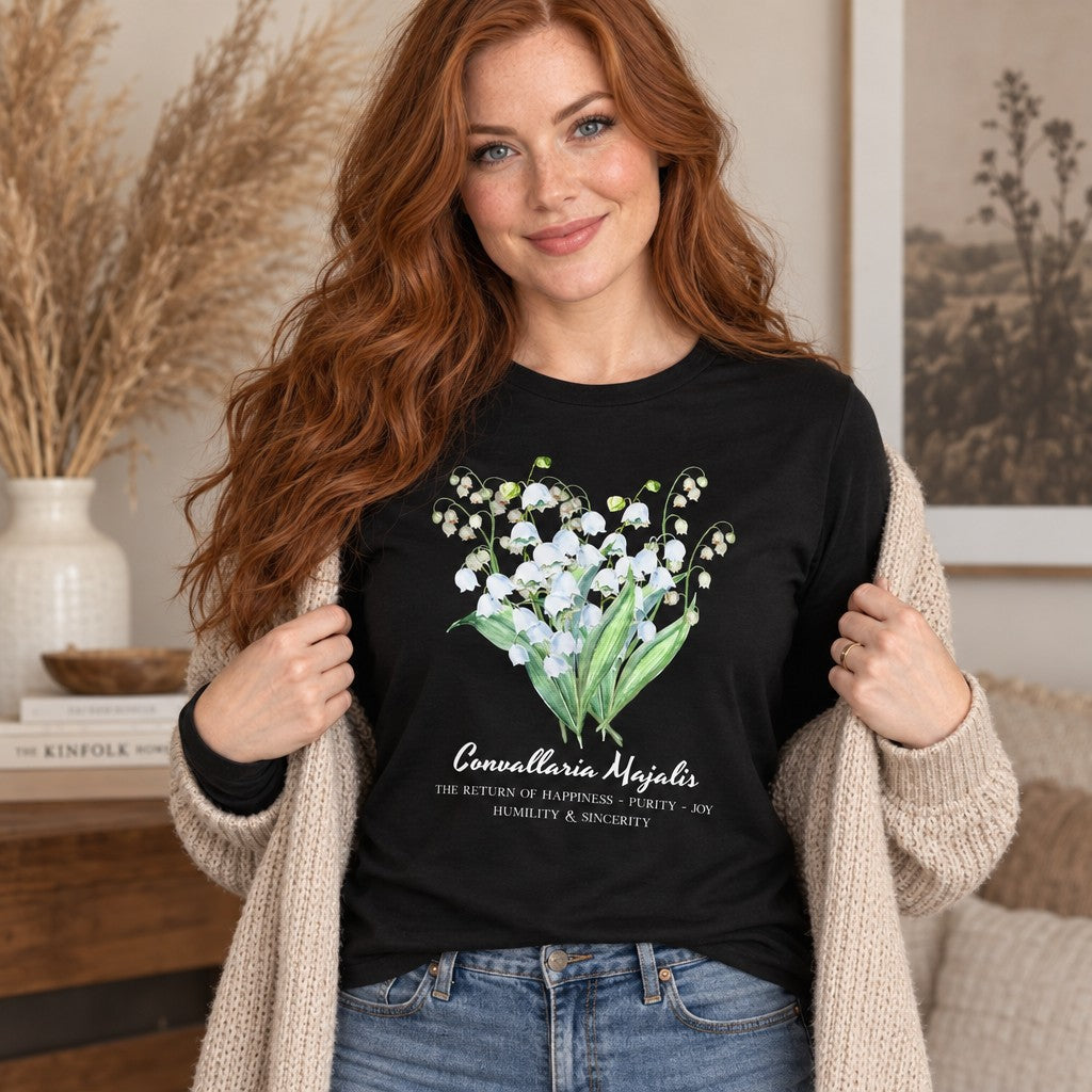 Red-haired woman wearing a black Bella Canvas 3501 long sleeve shirt with an ethereal watercolor lily of the valley botanical bouquet design, vintage cottagecore floral style, in a cozy cottage-inspired living room, perfect for women who love botanical art and garden aesthetics, by Crossroads Dandelion