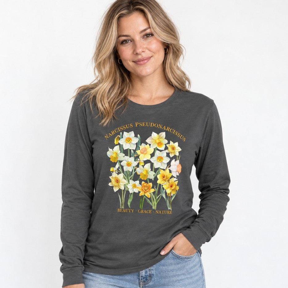 Woman wearing an asphalt Bella Canvas 3501 long sleeve shirt featuring a cottagecore watercolor daffodil botanical specimen design with elegant Latin script, perfect for garden lovers and creative women, by Crossroads Dandelion