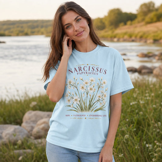 Woman wearing a chambray Comfort Colors 1717 t-shirt with a vintage cottagecore narcissus papyraceus floral watercolor design, standing by a scenic riverside, perfect for creative souls and nature-inspired cottagecore fashion, by Crossroads Dandelion