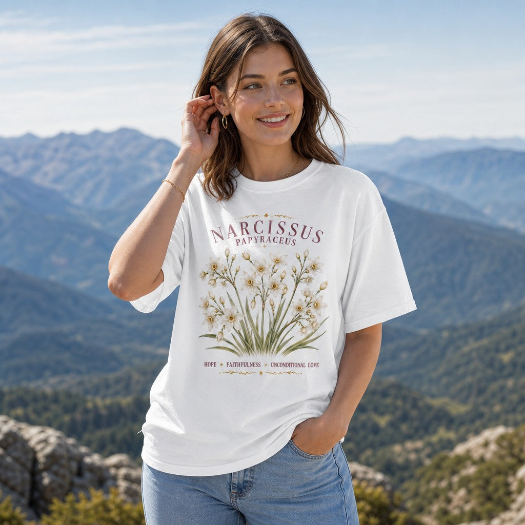 Woman in white Comfort Colors 1717 t-shirt featuring a vintage watercolor Narcissus papyraceus floral design with gold accents, standing in a scenic mountain setting, cottagecore aesthetic for creative women, by Crossroads Dandelion