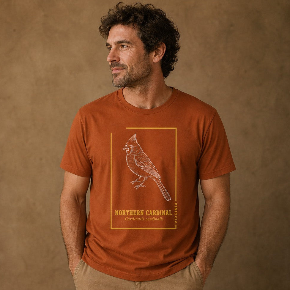 Man wearing an autumn orange Bella Canvas 3001 t-shirt featuring a white hand-drawn line art illustration of a northern cardinal framed by gold vintage accents and elegant serif text, cottagecore vintage style, ideal for birdwatchers and nature lovers, by Crossroads Dandelion