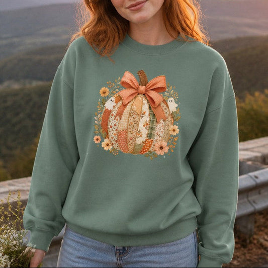 Woman wearing a light green Comfort Colors 1566 sweatshirt featuring a whimsical cottagecore patchwork pumpkin design with vintage florals, rustic plaids, a textured bow, surrounded by delicate autumn flowers and two cute ghosts, standing by mountain overlook at sunset, cozy fall apparel for women, by Crossroads Dandelion