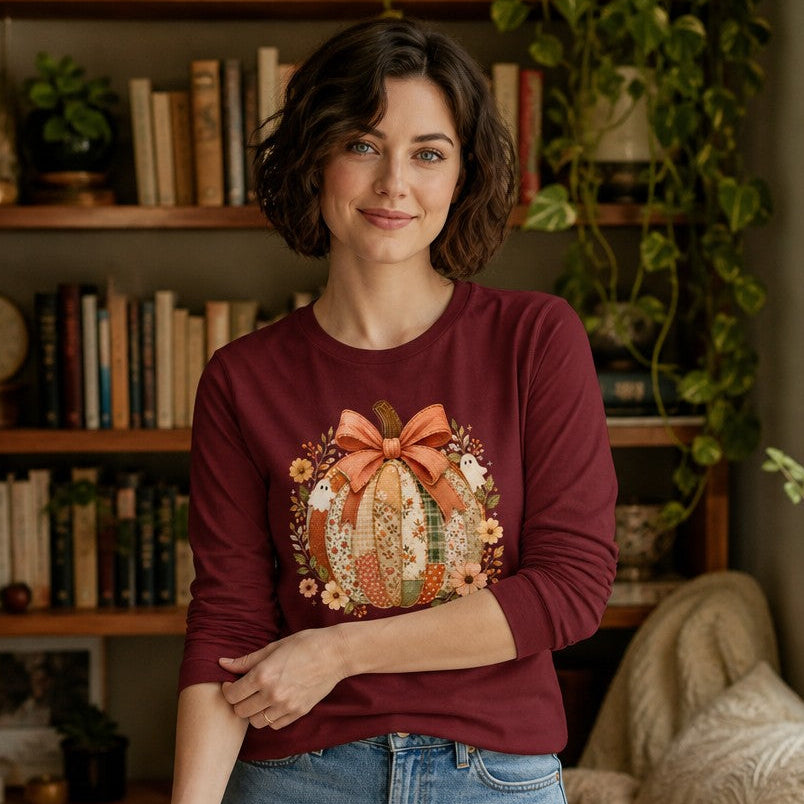 Woman in cardinal Bella Canvas 3501 long sleeve shirt featuring a whimsical patchwork pumpkin with floral crown, faded coral bow, vintage ghosts, sage and russet wildflowers, cozy living room, cottagecore autumn Halloween shirt for women, by Crossroads Dandelion
