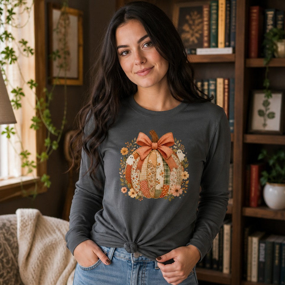 Woman in asphalt Bella Canvas 3501 long sleeve shirt featuring a whimsical cottagecore patchwork pumpkin design with florals and vintage-style ghosts, cozy home library setting, ideal for autumn and Halloween lovers, by Crossroads Dandelion