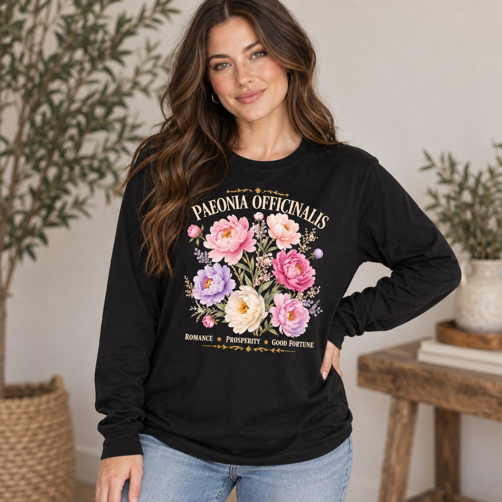 Woman wearing a black Bella Canvas 3501 long sleeve tee featuring a romantic watercolor peony and wildflower design with vintage botanical script, cottagecore style, garden-inspired for botanical lovers, photographed indoors, by Crossroads Dandelion