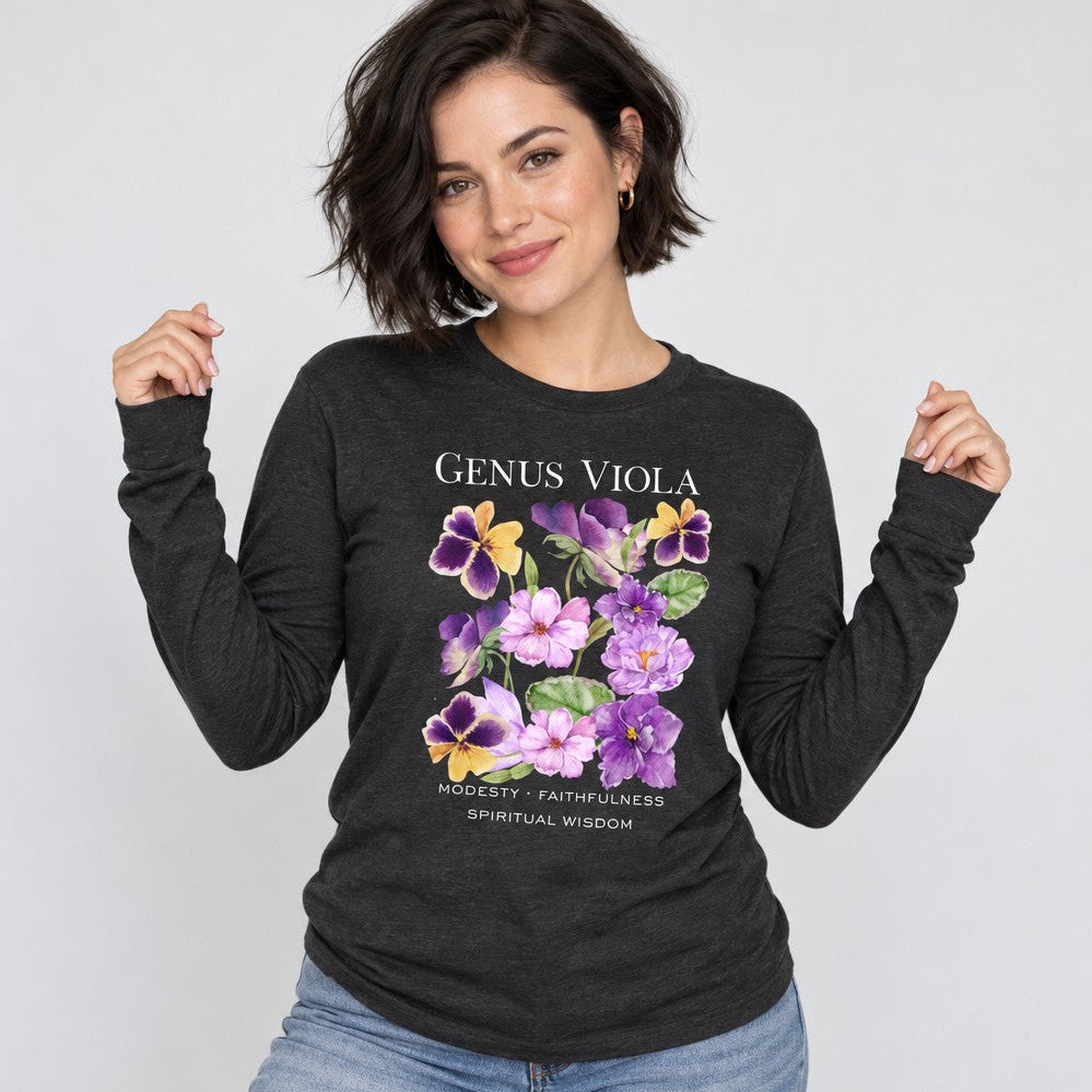 Woman wearing dark grey heather Bella Canvas 3501 long sleeve shirt with a cottagecore watercolor design of violets, pansies, and heart-shaped leaves, vintage nature journal style with hand-lettered botanical symbolism for modesty, faithfulness, and spiritual wisdom, perfect for botanical art lovers, by Crossroads Dandelion
