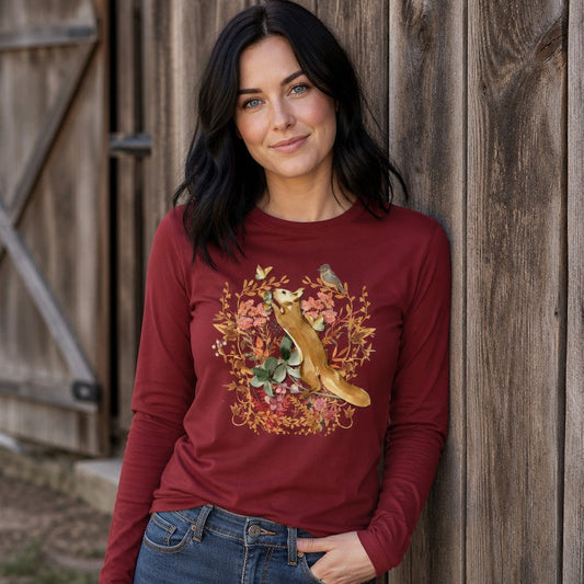 Woman wearing a cardinal red Bella Canvas 3501 long sleeve shirt with a vintage watercolor fox, wildflowers, butterflies, and songbird design, standing by a rustic barn, cottagecore and nature lovers apparel, by Crossroads Dandelion