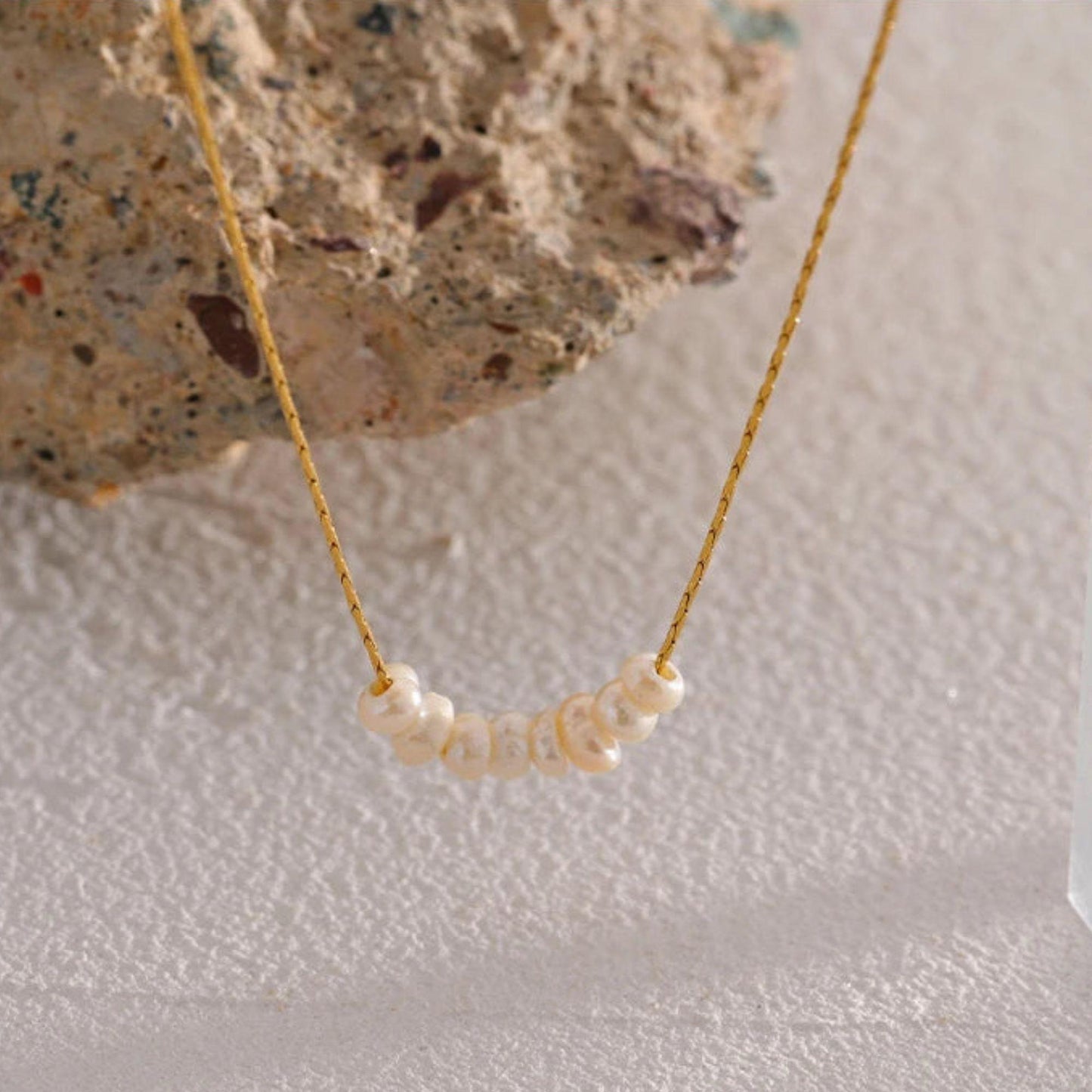 Close-Up of a Minimalist pearl bar necklace on gold pleated chain on organic background