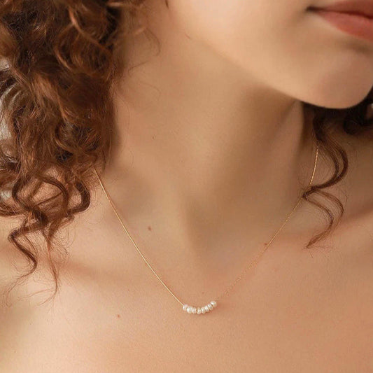 Close-up of a woman wearing a delicate gold necklace with small natural pearls.