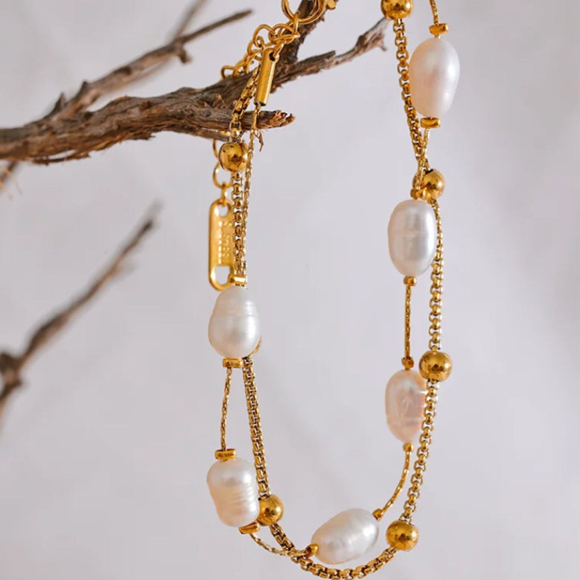 Double layer freshwater pearl bracelet with gold ball beads on stainless steel gold plated box chain, white background with branch by Crossroads Dandelion