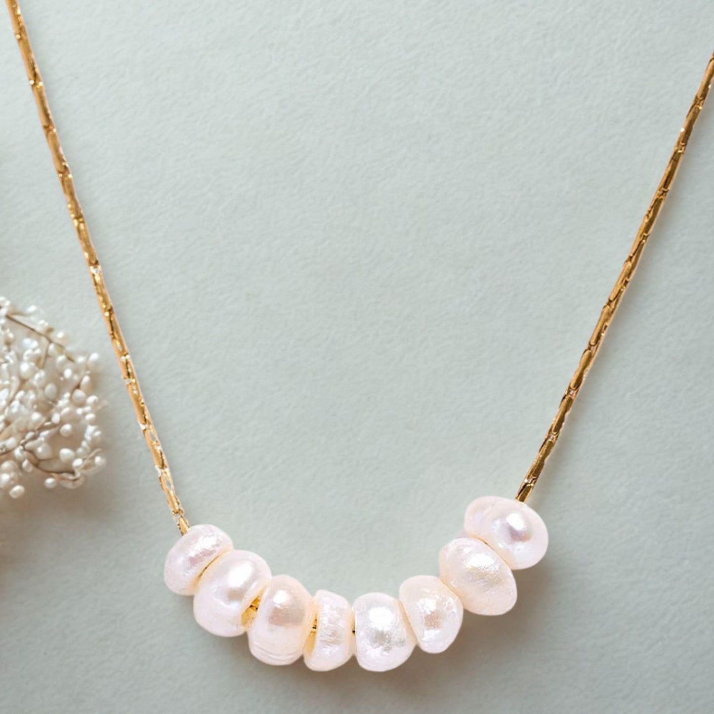 Close-up of a natural pearl necklace with gold pleated chain on a light green background