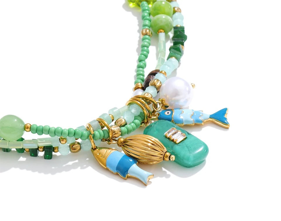 Close up of a colorful beaded necklace with fish-shaped charms on a white background by Crossroads Dandelion