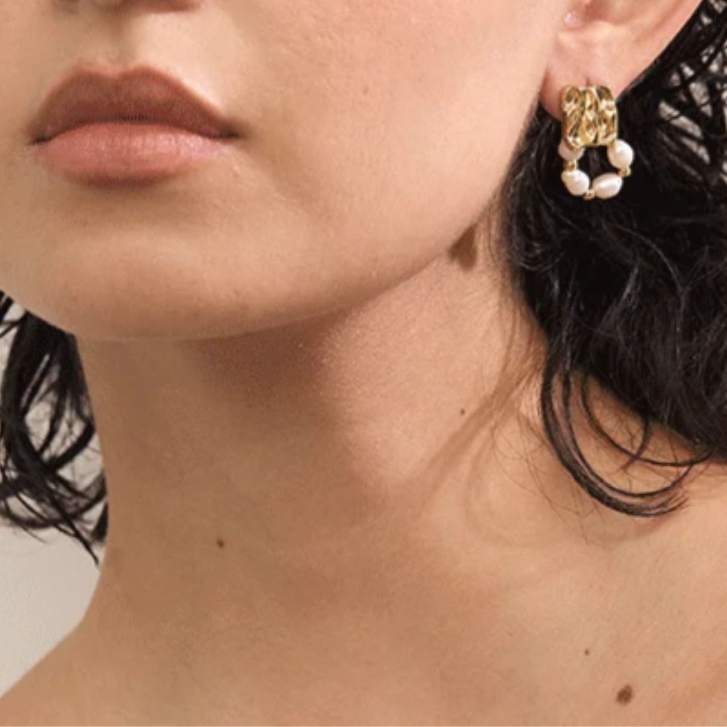 Close-up of freshwater baroque pearl drop earrings in gold PVD plated stainless steel worn on ear, geometric textured square stud with pearl hoop loop, by Crossroads Dandelion