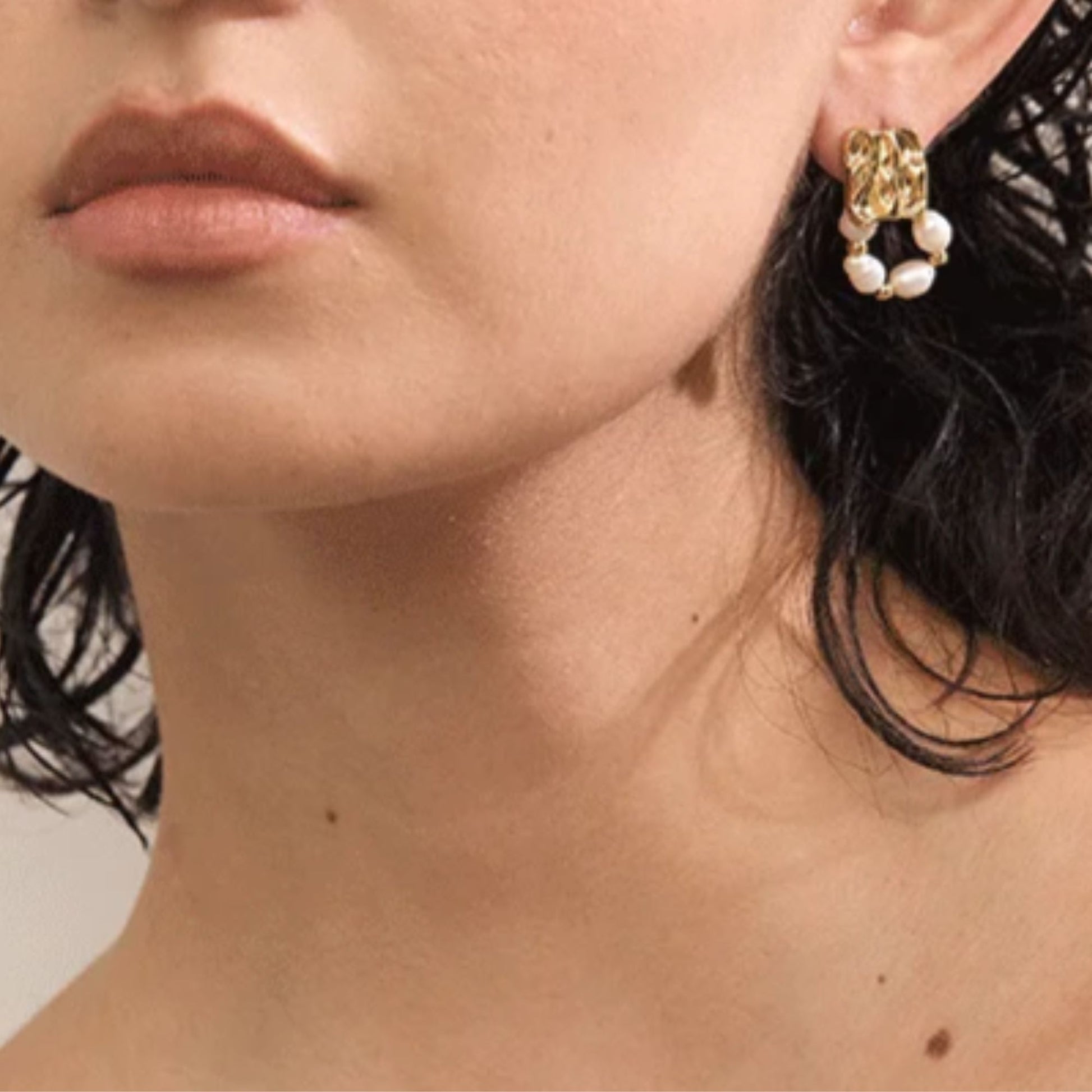 Close-up of freshwater baroque pearl drop earrings in gold PVD plated stainless steel worn on ear, geometric textured square stud with pearl hoop loop, by Crossroads Dandelion