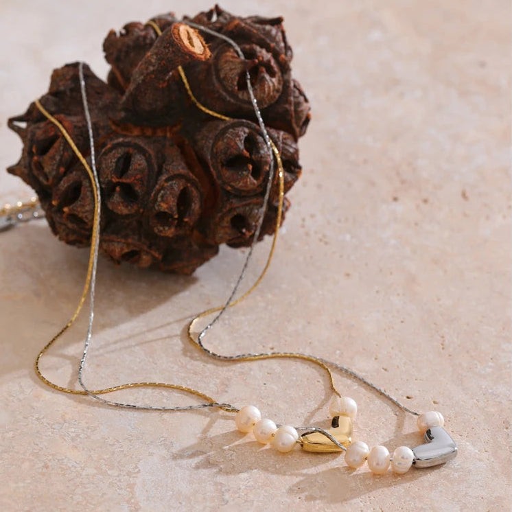Gold and silver pearl heart necklaces on stone beside a dried seed pod