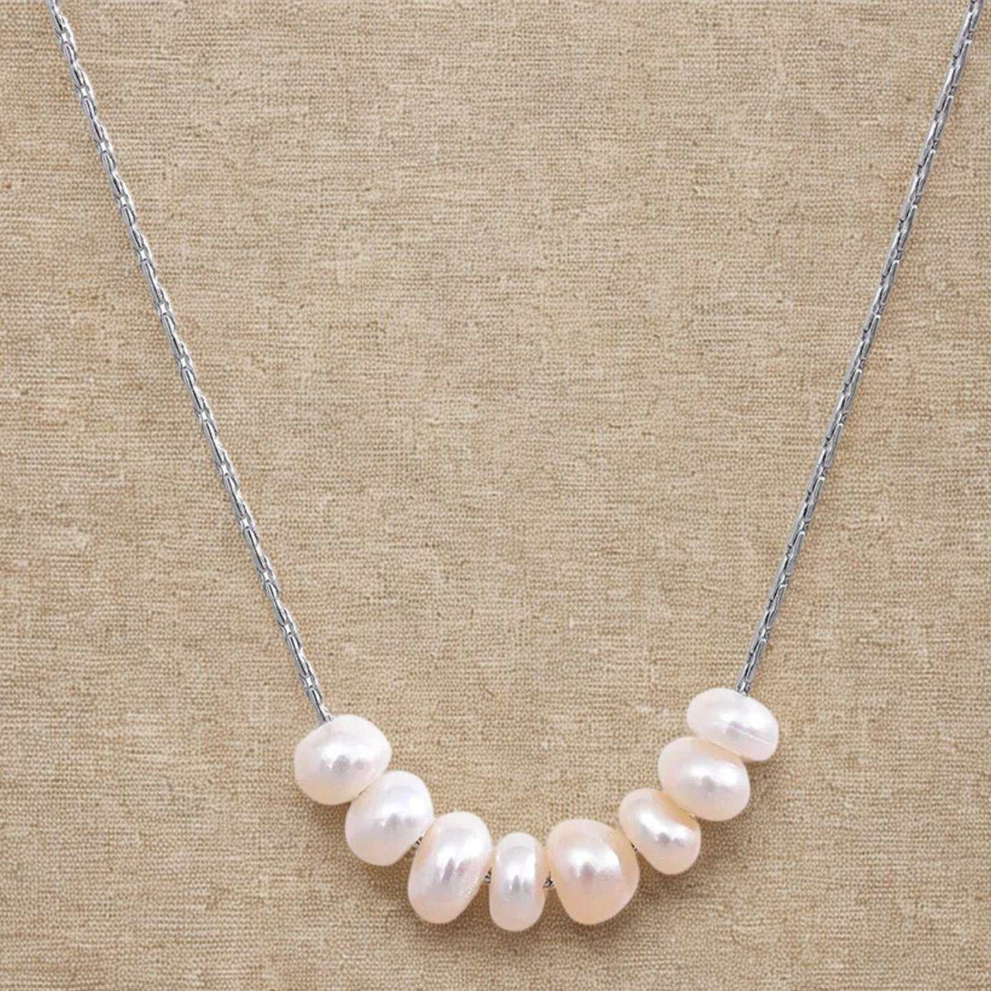 Close-up of a natural pearl necklace with stainless steel chain on a linen background