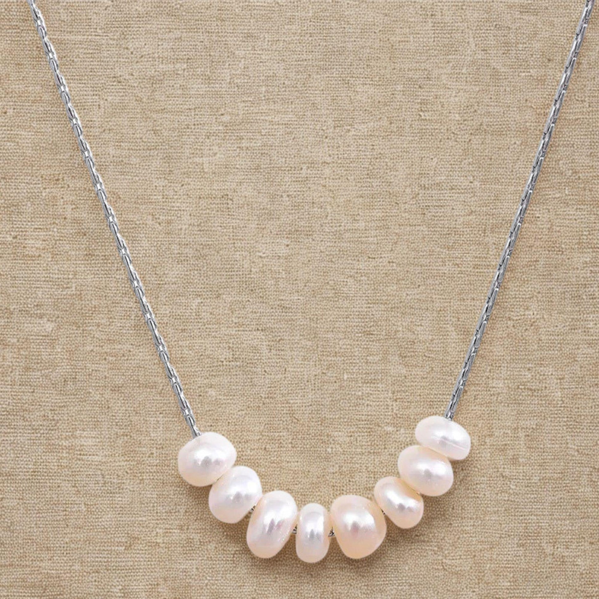 Close-up of a natural pearl necklace with stainless steel chain on a linen background
