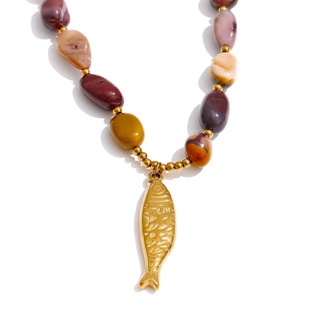 Engraved gold fish pendant hanging from earthy natural stone beads, front view on white
