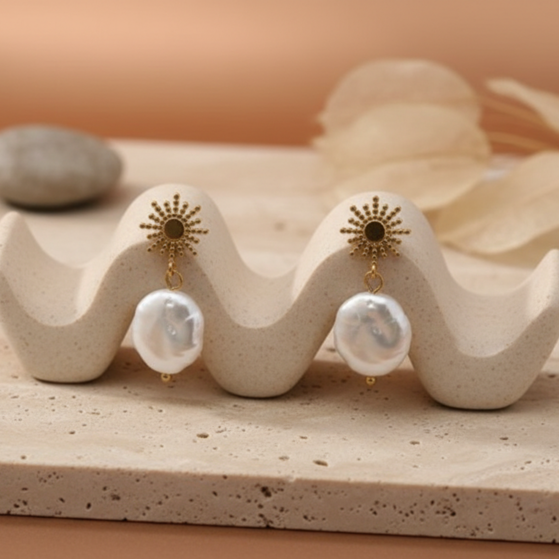 Gold pearl drop earrings displayed on ceramic holder with warm tones, minimalist product photography, by Crossroads Dandelion