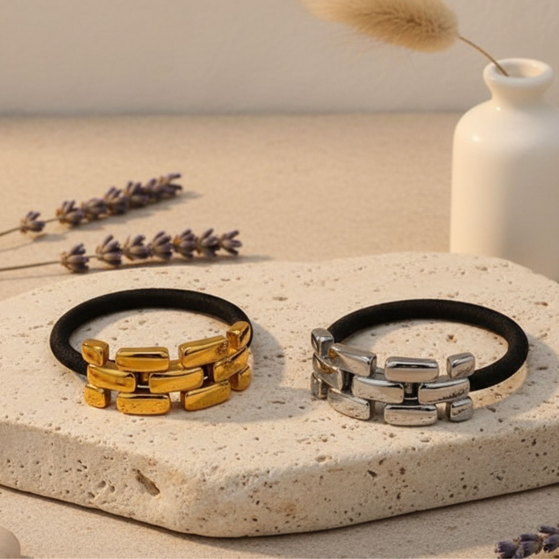 Two hair bands, one gold and one stainless steel, on a stone surface with lavender and a vase in the background.