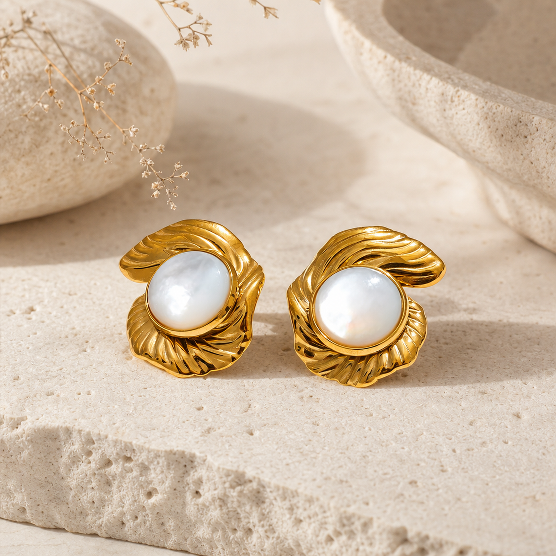 Elegant gold and pearl stud earrings displayed on a textured natural stone surface with dried floral accents, product mockup, by Crossroads Dandelion