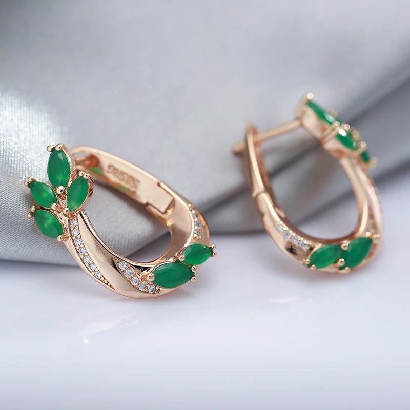 Close-up of green leaf hoop earrings in rose gold beside silver satin