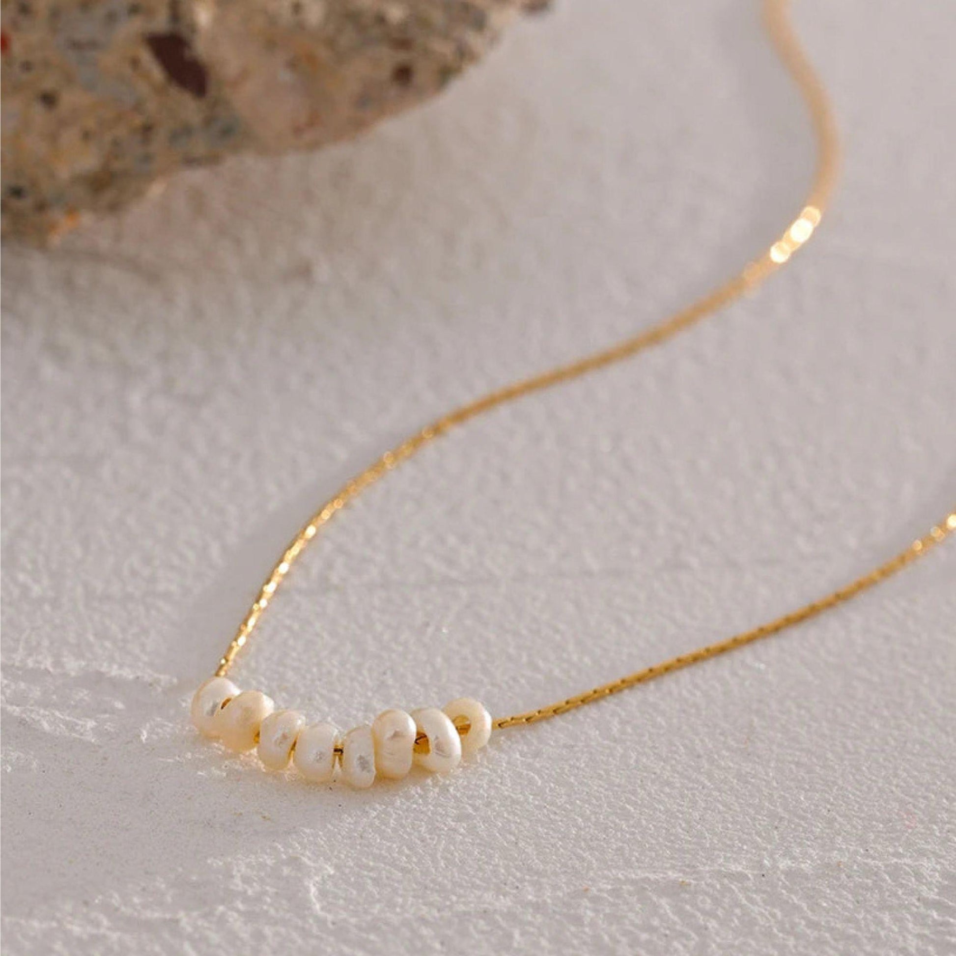 Gold pleated necklace with pearls on a light organic background