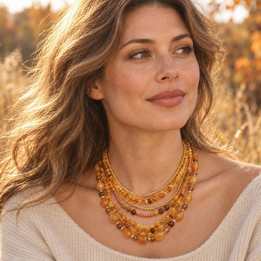 Woman in a cream knit wearing a honey layered beaded bib necklace in a golden autumn field