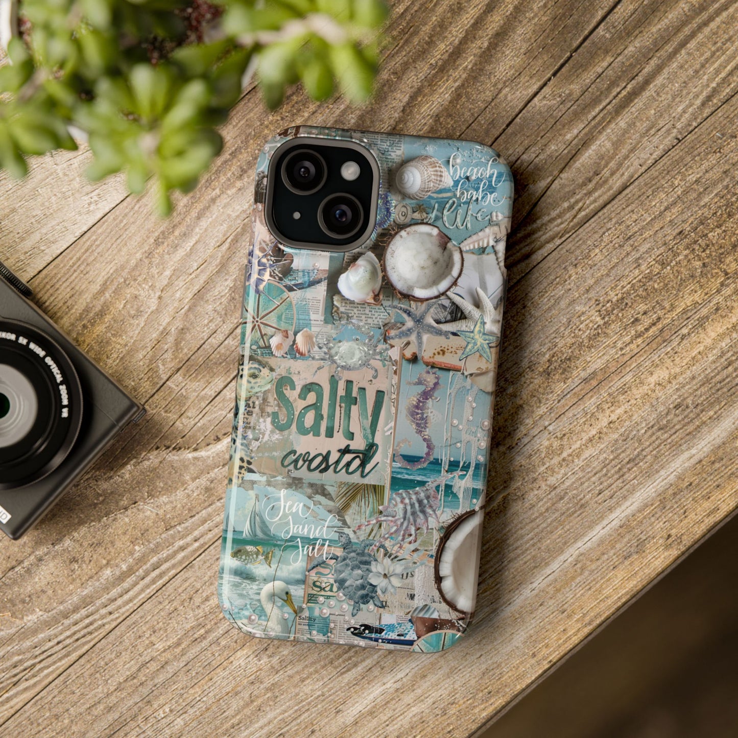 Salty Coastal vintage beach iPhone 15 Plus glossy phone case mockup with seashell collage artwork on rustic tabletop scene, by Crossroads Dandelion

