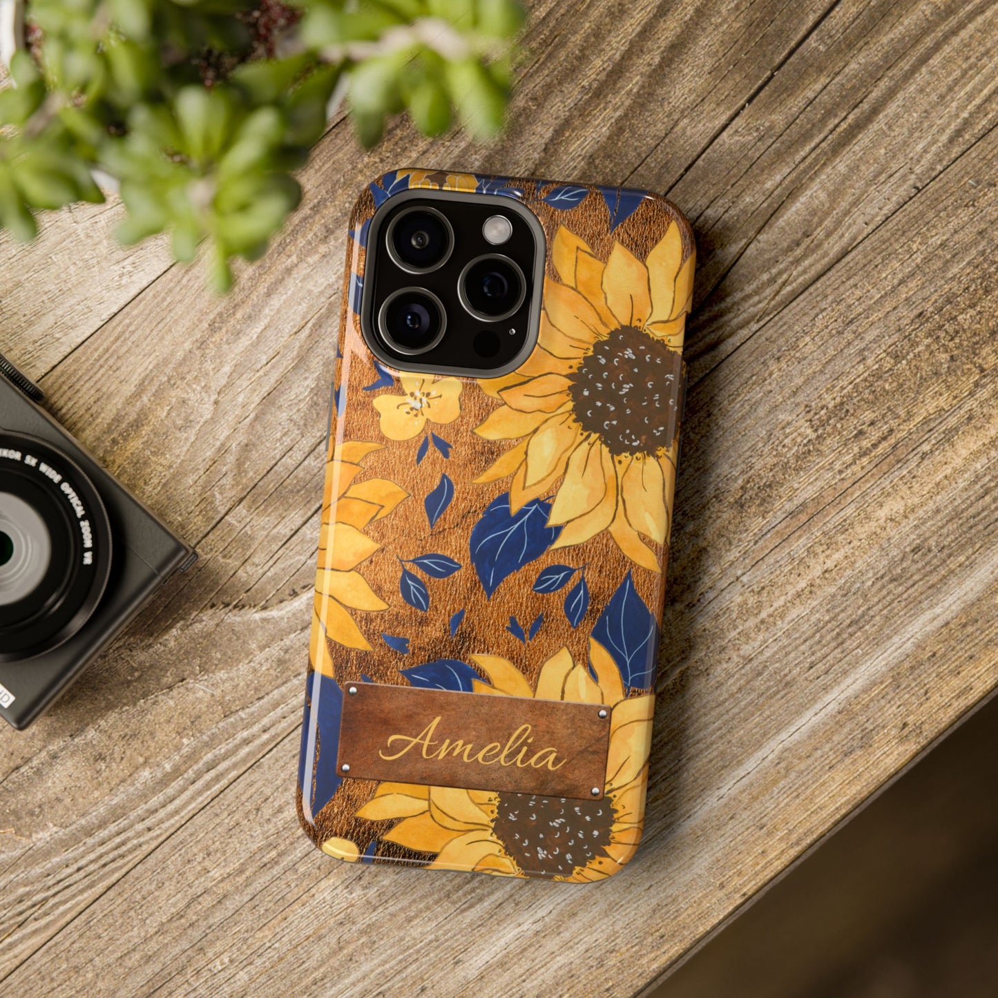 Custom name personalized sunflower western tough phone case for iPhone 15 Pro Max, featuring bold yellow sunflowers, navy blue leaves, rustic brown faux leather texture background, and a riveted metal name plate — perfect boho cowgirl gift, by Crossroads Dandelion