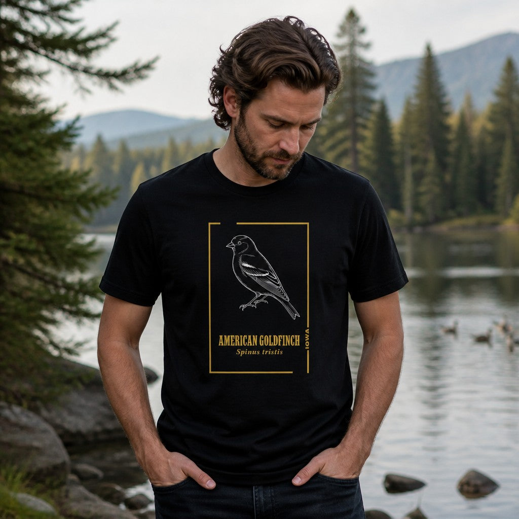 Man wearing a black Bella Canvas 3001 t-shirt with a vintage line art illustration of an American Goldfinch perched amid golden botanical accents, nature-themed typography, standing by a serene forest lake, perfect for bird watchers, naturalist art lovers, and men seeking heritage-inspired apparel, by Crossroads Dandelion
