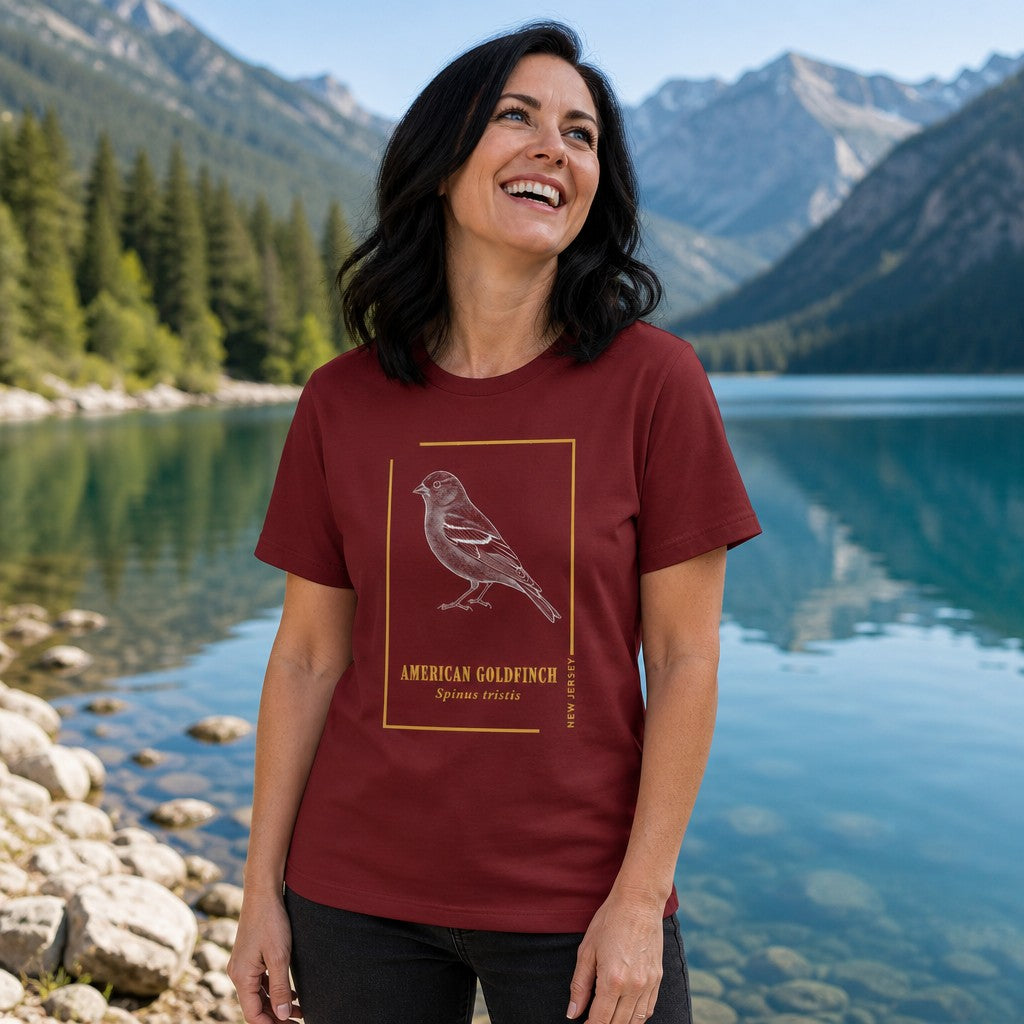 Woman wearing cardinal red t-shirt with vintage line art American goldfinch bird design, standing by a mountain lake with pine trees, ideal for bird watchers and outdoor lovers, by Crossroads Dandelion