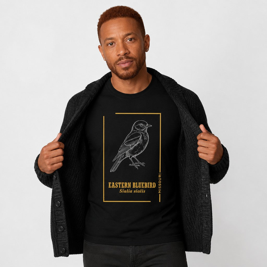 Man wearing a black Bella Canvas 3001 t-shirt featuring an intricate white line art illustration of an Eastern Bluebird with golden vintage botanical accents and scientific name, vintage field guide style for birdwatchers and nature lovers, by Crossroads Dandelion