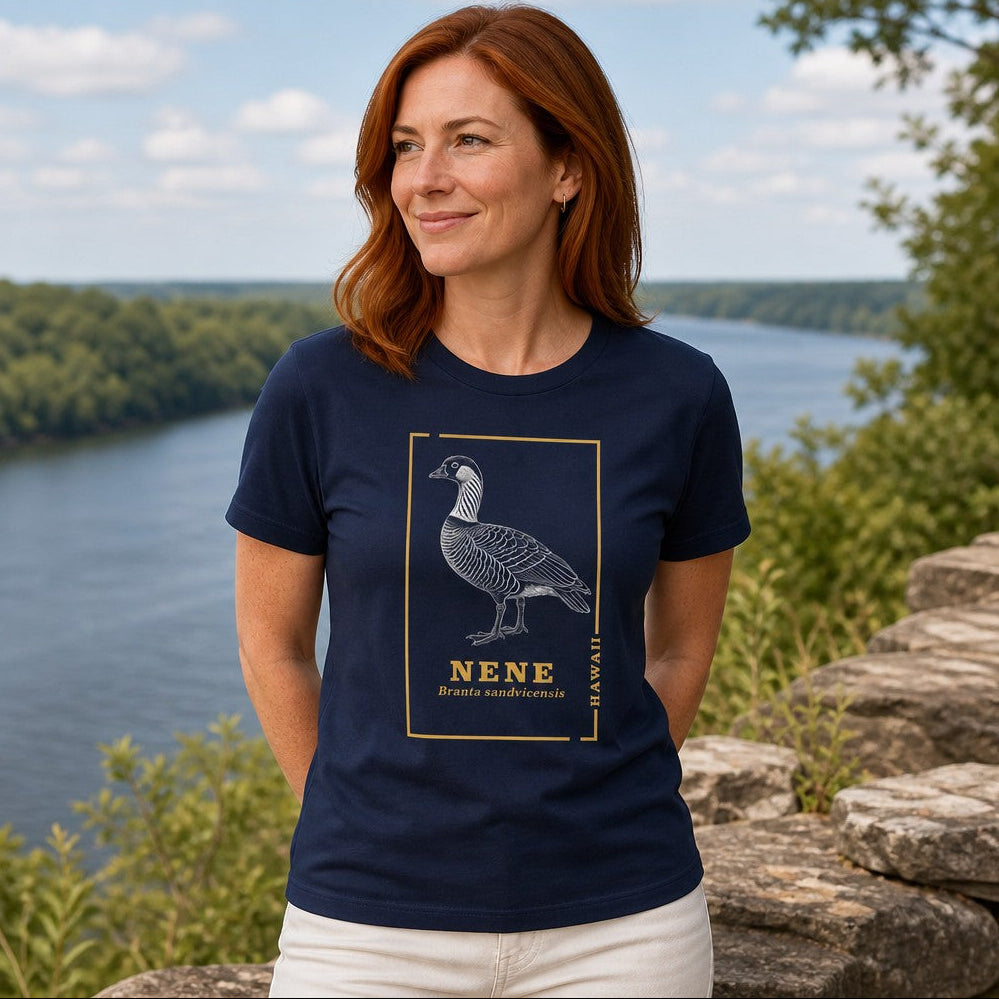 Woman wearing a navy t-shirt featuring a line art design of the Hawaiian nene goose with scientific name branta sandvicensis, standing by a river, outdoor nature scene, perfect for bird lovers and nature enthusiasts, by Crossroads Dandelion