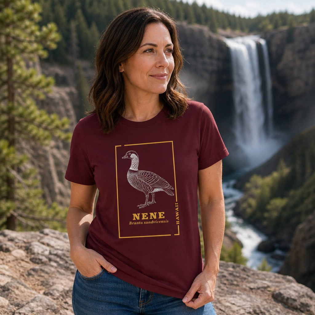 Woman in maroon t-shirt featuring a line art design of the Hawaiian nene goose with scientific name, standing by a waterfall in a pine forest, perfect for birdwatchers and nature lovers, by Crossroads Dandelion