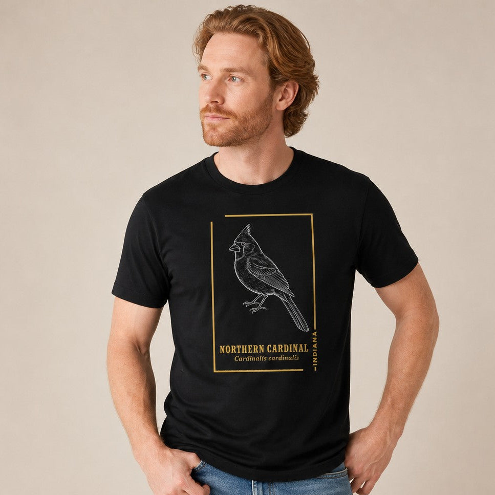 Man wearing a black Bella Canvas 3001 t-shirt featuring a vintage-inspired line art illustration of a Northern Cardinal with goldenrod frame and classic field guide typography, ideal for wildlife art and birdwatching enthusiasts, timeless style for men, by Crossroads Dandelion