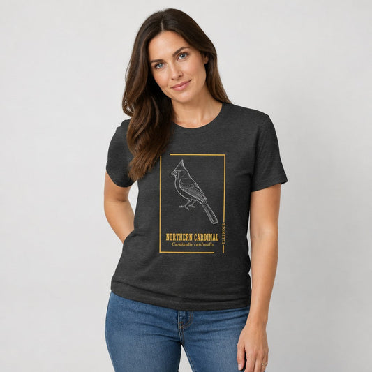 Woman wearing a dark grey heather Bella Canvas 3001 t-shirt with vintage white line art northern cardinal illustration, golden minimalist frame, antique botanical typography, for birders and nature lovers, by Crossroads Dandelion