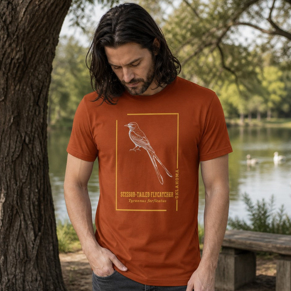 Man wearing an autumn orange Bella Canvas 3001 t-shirt featuring a vintage-inspired line art drawing of a scissor-tailed flycatcher within a golden frame, set in a serene lakeside park, for bird watchers, wildlife lovers, and naturalists, by Crossroads Dandelion