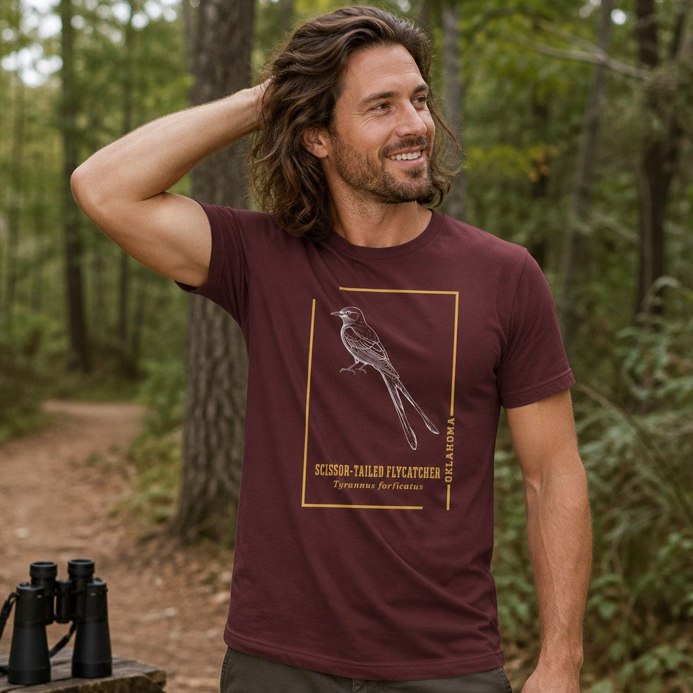 Man wearing a maroon Bella Canvas 3001 t-shirt featuring a vintage-inspired line art scissor-tailed flycatcher within a golden frame, perfect for bird lovers and nature enthusiasts, styled for tranquil hiking in the forest, by Crossroads Dandelion
