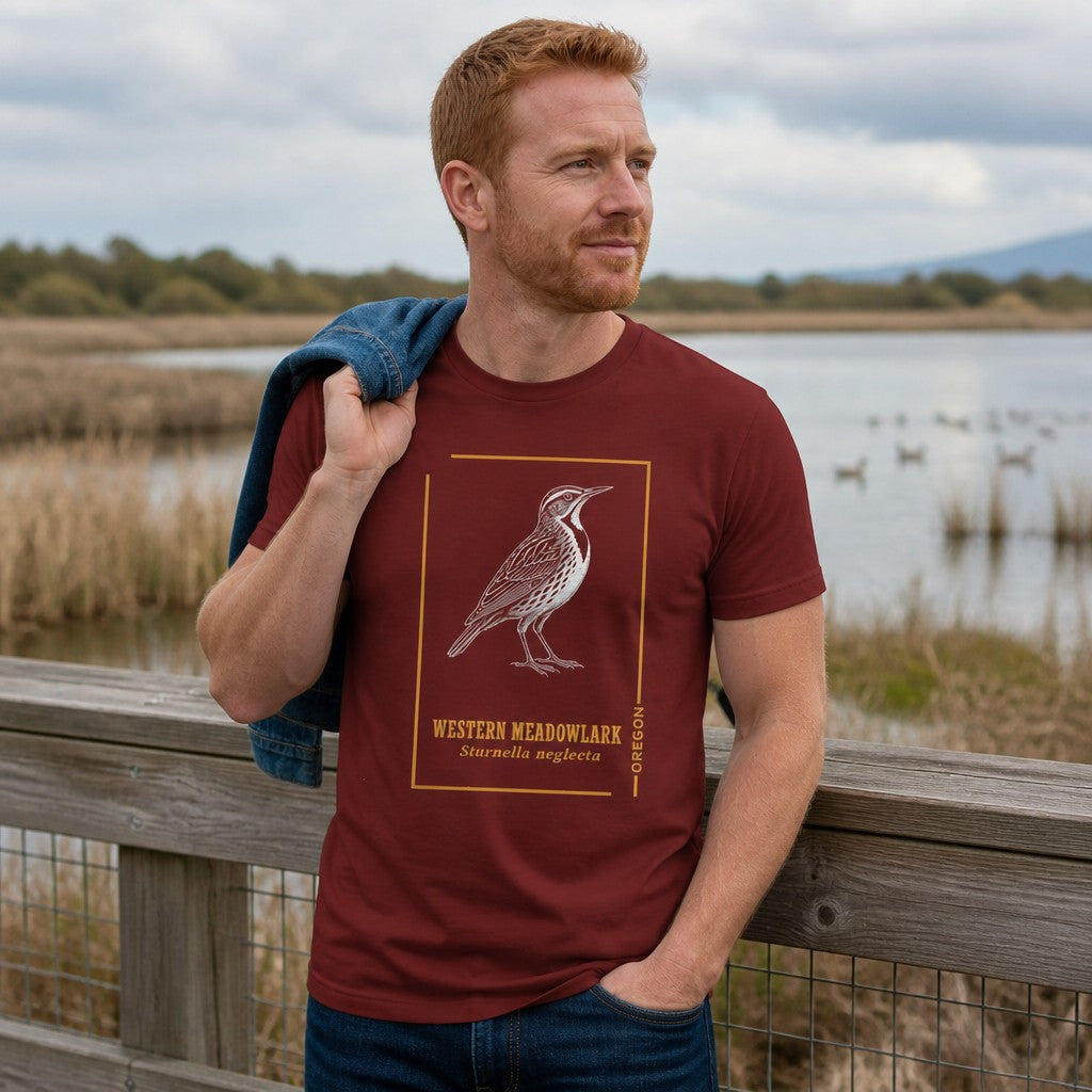 Man wearing cardinal Bella Canvas 3001 t-shirt with an intricate line art Western Meadowlark design framed in golden ochre, evoking vintage field guides and botanical journals, perfect for Oregon nature lovers and birdwatchers, outdoor marsh scene, by Crossroads Dandelion