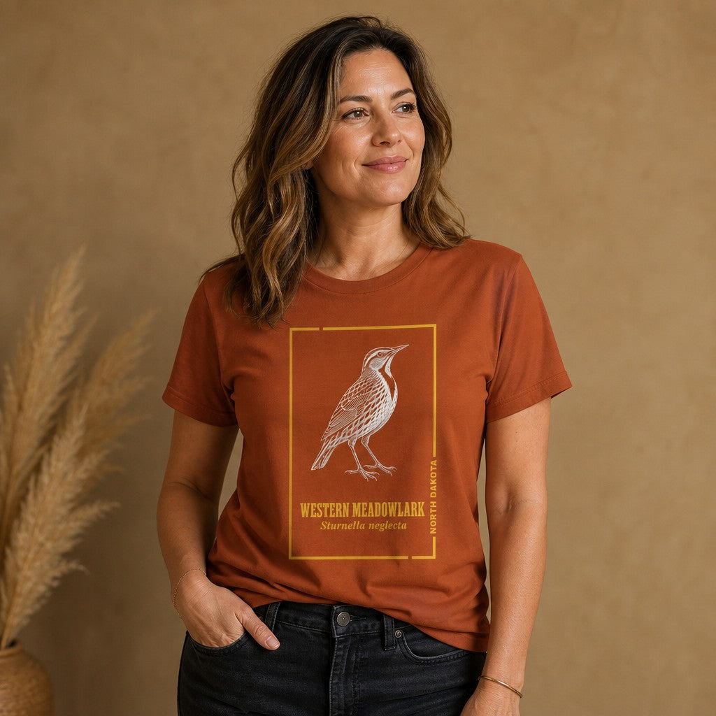 Woman wearing an autumn-colored Bella Canvas 3001 t-shirt with intricate line art of a western meadowlark and vintage scientific labeling, ideal for birdwatchers and nature lovers, casual studio setting, by Crossroads Dandelion
