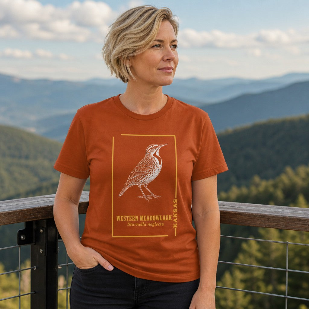 Woman wearing an autumn color t-shirt with a line art western meadowlark bird design and Arkansas text, standing on a scenic mountain overlook, outdoor nature lover style, for women, by Crossroads Dandelion