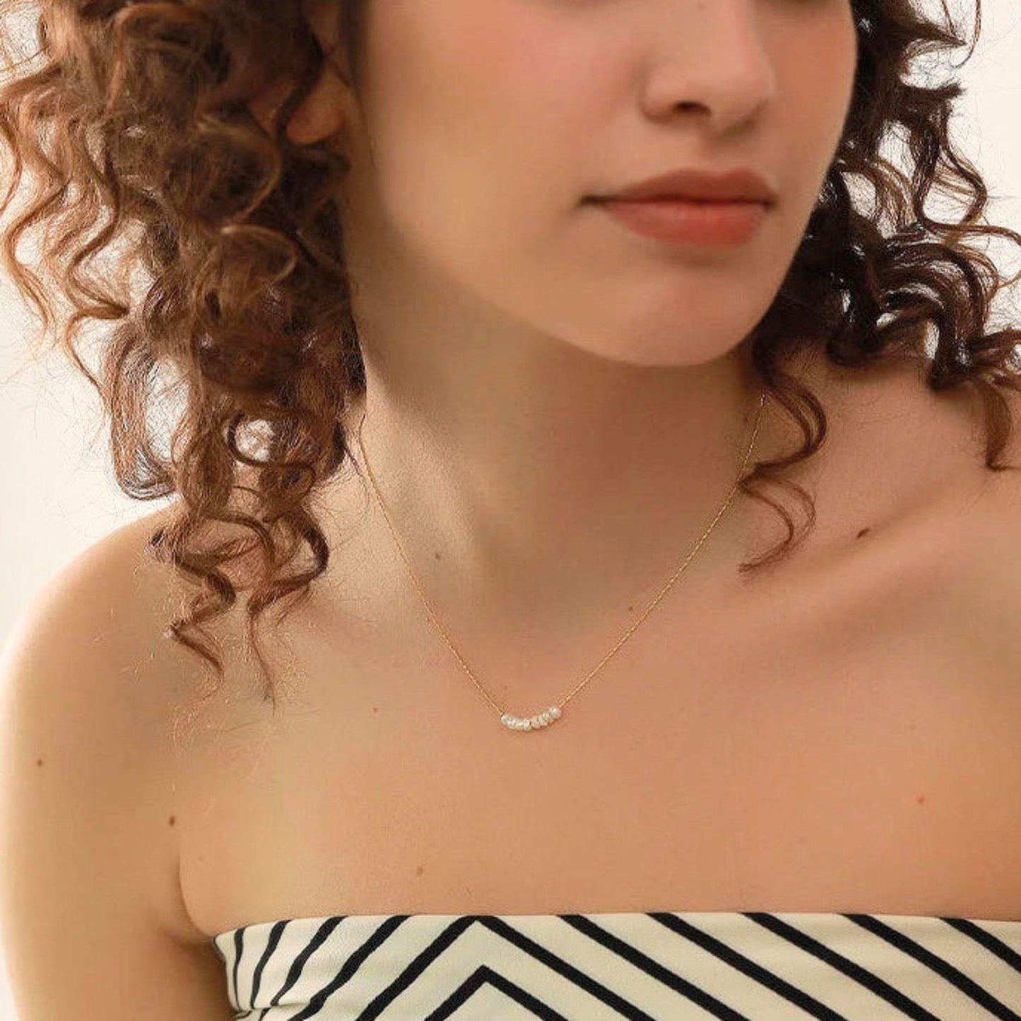 Close-up of a woman wearing a delicate necklace with a neutral background