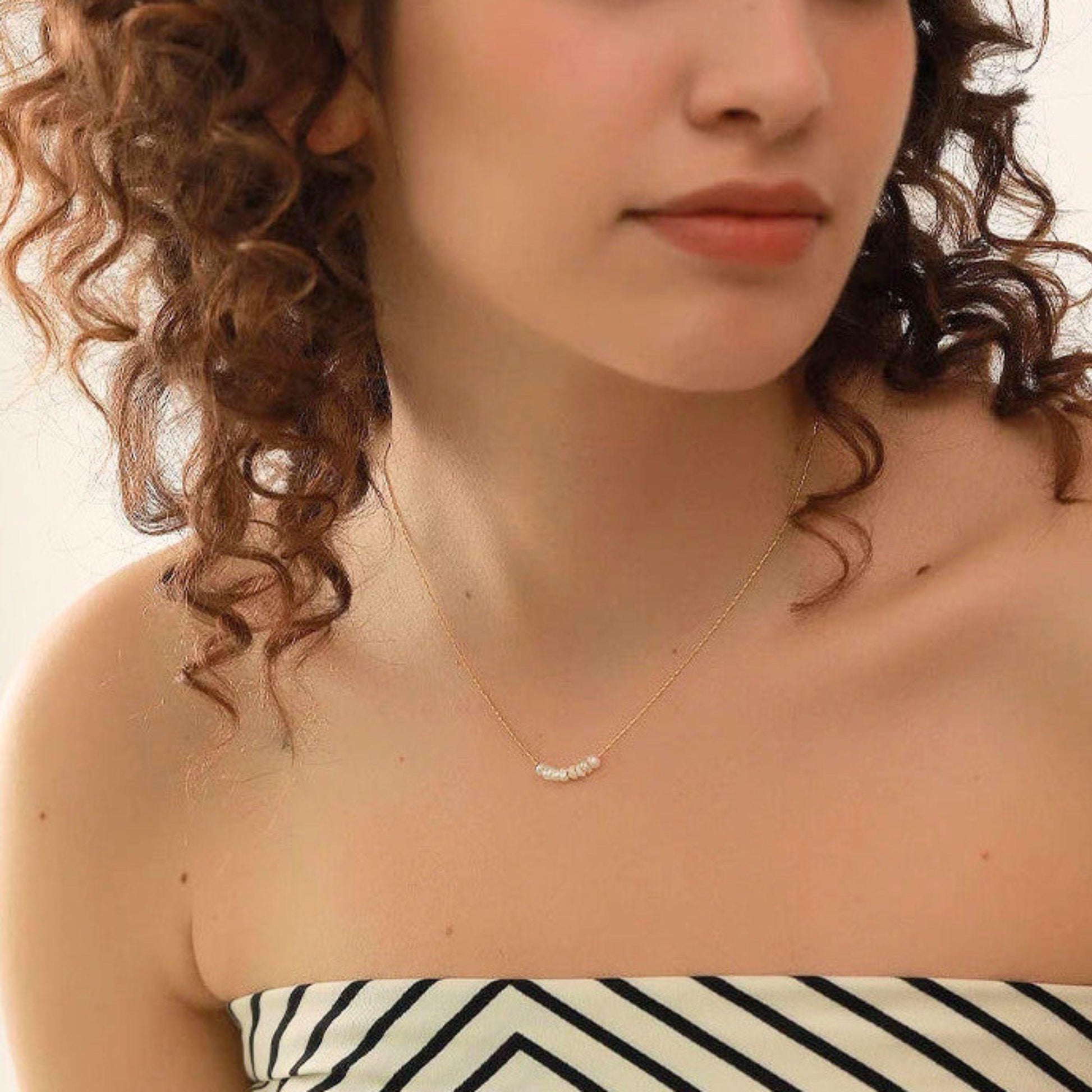Close-up of a woman wearing a delicate necklace with a neutral background
