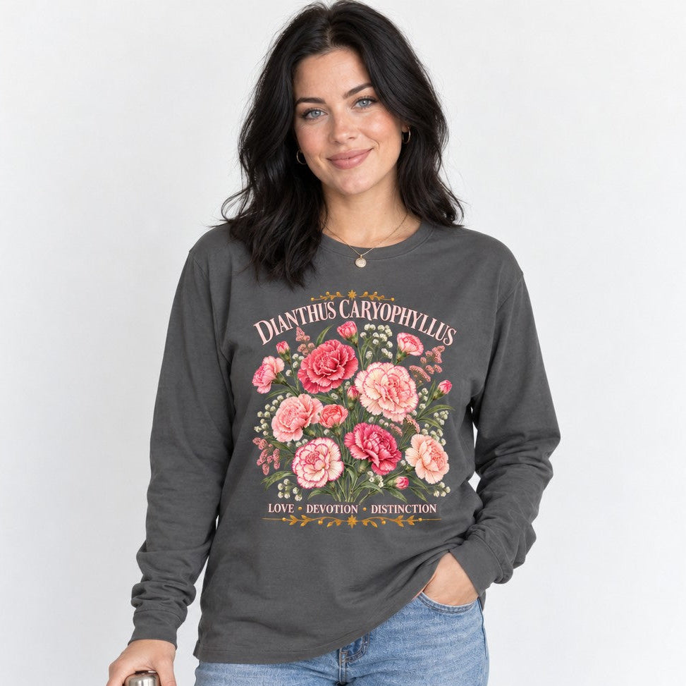Woman wearing an asphalt Bella Canvas long sleeve with a vintage cottagecore watercolor illustration of pink and blush carnations, labeled 'DIANTHUS CARYOPHYLLUS' and 'LOVE · DEVOTION · DISTINCTION,' ideal for garden and flower lovers, by Crossroads Dandelion