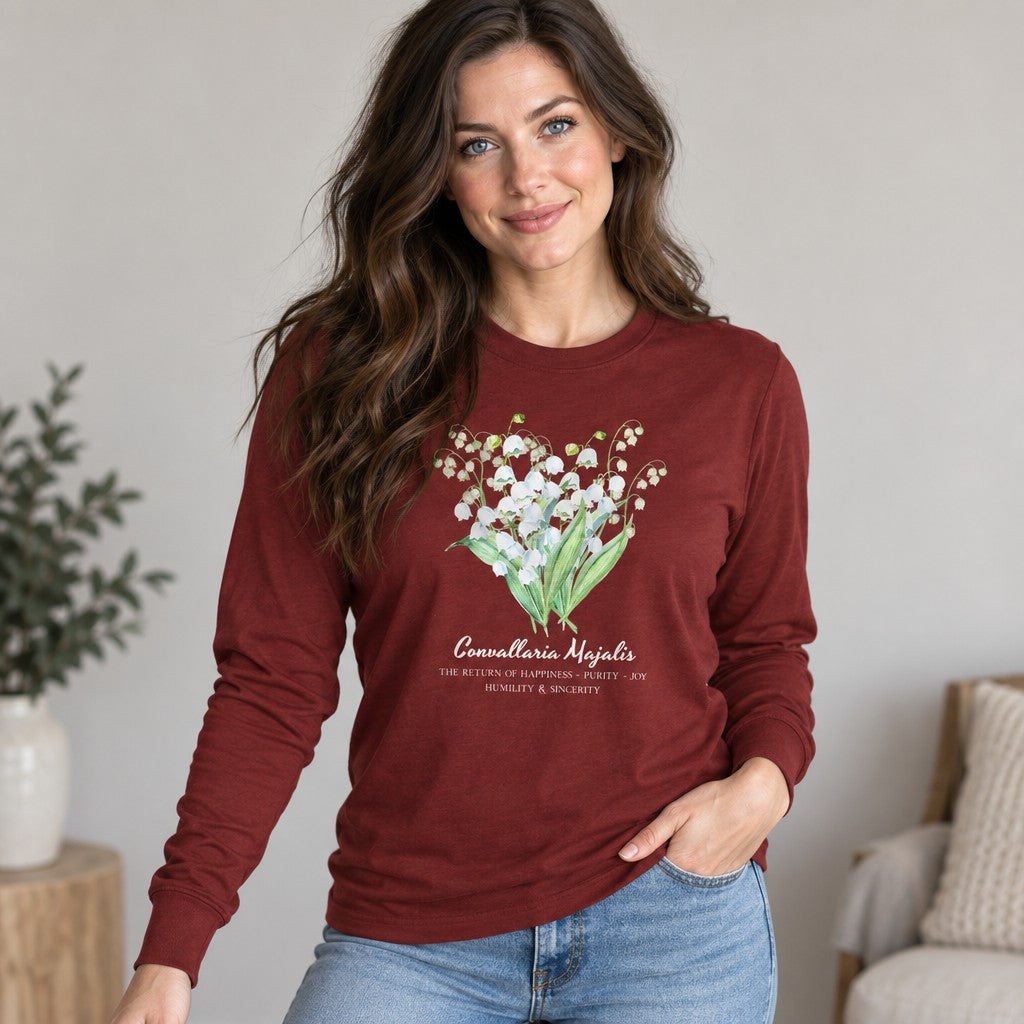 Woman in cardinal red Bella Canvas 3501 long sleeve shirt featuring a vintage cottagecore watercolor bouquet of lily of the valley, perfect for botanical art and floral illustration lovers, relaxed home setting, by Crossroads Dandelion
