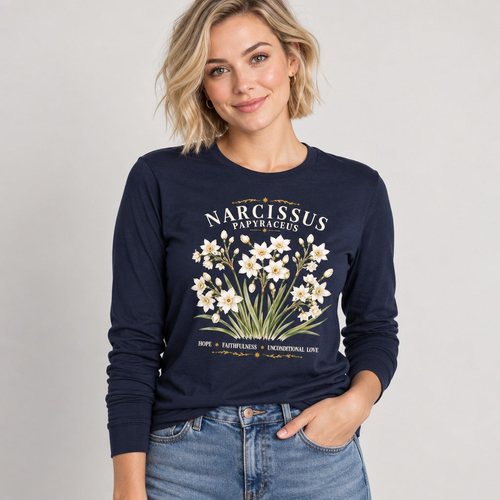 Woman wearing a navy Bella Canvas 3501 long sleeve shirt featuring a vintage botanical illustration of white narcissus papyraceus flowers with elegant serif typography and gold ornamental accents, classic and sentimental floral design for garden lovers, by Crossroads Dandelion