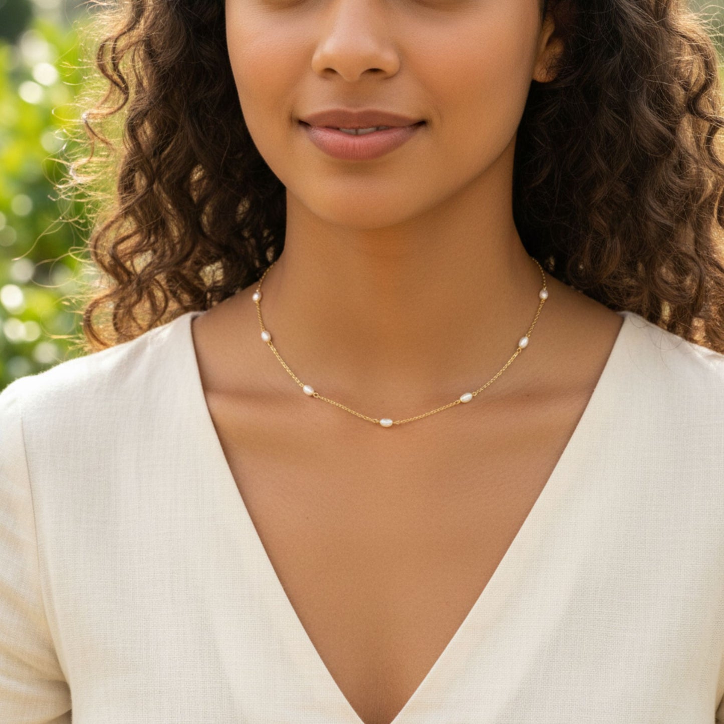Close-up of a woman wearing a delicate station necklace with small natural pearls.